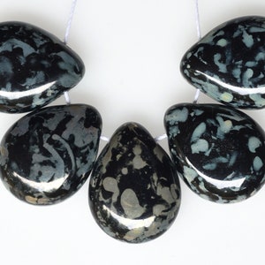 May include: A strand of five teardrop-shaped beads. The beads are primarily black with a pattern of gray and white inclusions. They are strung on a white cord, and the beads have a polished, glossy finish.