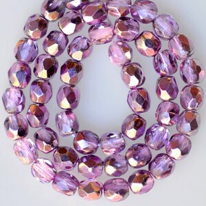 May include: A strand of iridescent purple glass beads with a faceted finish. The beads are arranged in a circular pattern, creating a shimmering effect.