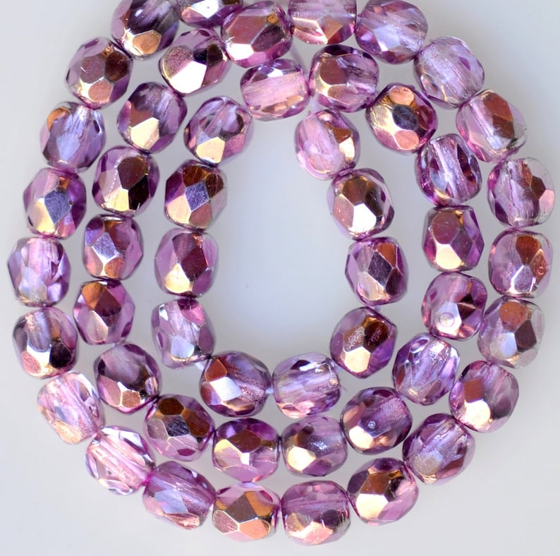 May include: A strand of iridescent purple glass beads with a faceted finish. The beads are arranged in a circular pattern, creating a shimmering effect.