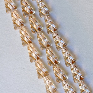 Puede incluir: Una hebra de cuentas de vidrio transparente con un patrón de espiral. Las cuentas tienen forma de triángulos y están dispuestas en filas.