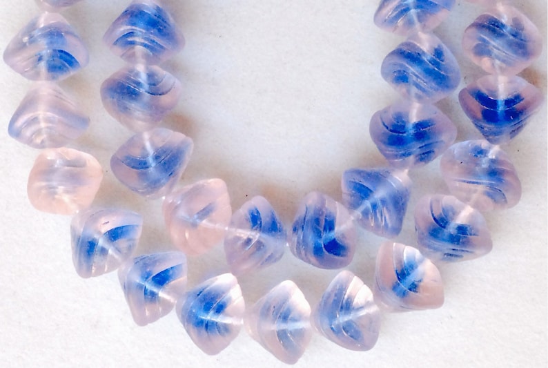 May include: A strand of light pink and blue glass beads. The beads are faceted and have a swirl design.