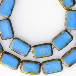May include: A strand of blue glass beads with a gold metallic rim. The beads are rectangular in shape and have a slightly iridescent finish.