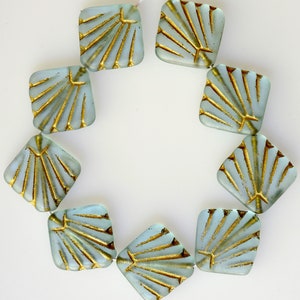 May include: A strand of ten square-shaped glass beads with a light blue color and gold accents. The beads have a sunburst design.