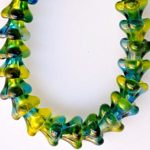 Puede incluir: Un collar hecho de cuentas de vidrio verde y azul. Las cuentas tienen forma de flor con un centro puntiagudo.