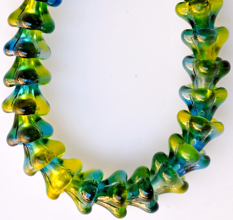 Puede incluir: Un collar hecho de cuentas de vidrio verde y azul. Las cuentas tienen forma de flor con un centro puntiagudo.