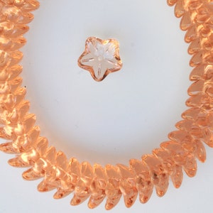 May include: A close-up of a peach-colored glass bead necklace with a clear star-shaped bead in the center.