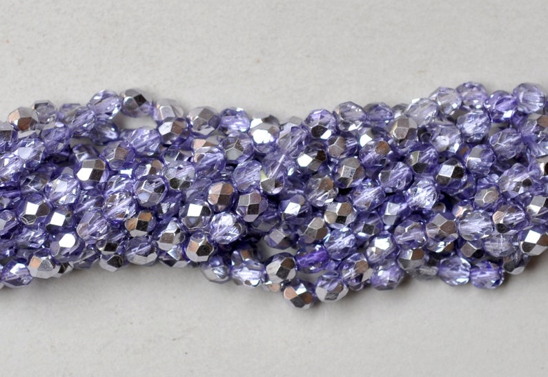 May include: A strand of iridescent purple glass beads with a faceted finish. The beads are small and round, and they have a metallic sheen.