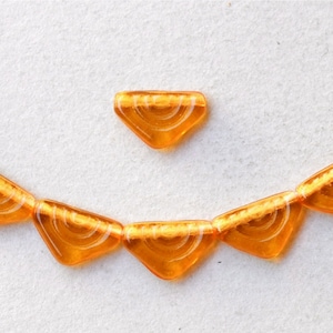 Puede incluir: Una hebra de cuentas de vidrio naranja con un diseño de espiral blanco. Las cuentas son de forma triangular y tienen un acabado brillante.