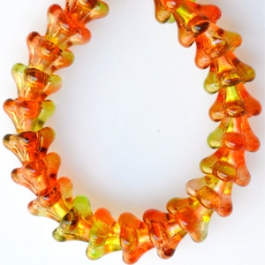 Puede incluir: Una hebra de cuentas de vidrio naranja y verde en forma de flor. Las cuentas est&aacute;n enhebradas para formar un collar o una pulsera.