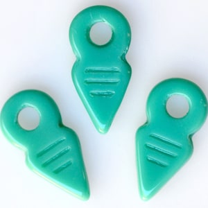 May include: Three teal blue glass pendant charms with a pointed tip and a small hole at the top. Each charm has three horizontal lines etched into the surface.