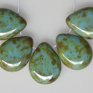 May include: Five teardrop-shaped beads strung on white thread. The beads are a mix of turquoise and brown, with a glossy finish. The beads are likely for jewelry making.