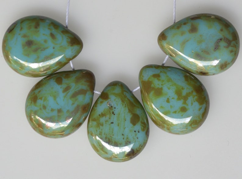 May include: Five teardrop-shaped beads strung on white thread. The beads are a mix of turquoise and brown, with a glossy finish. The beads are likely for jewelry making.