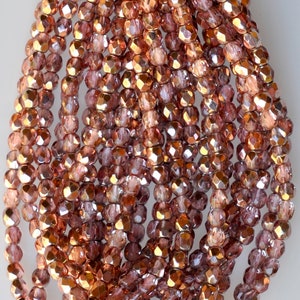 May include: A strand of rose gold glass beads with a faceted finish. The beads are small and have a metallic sheen.
