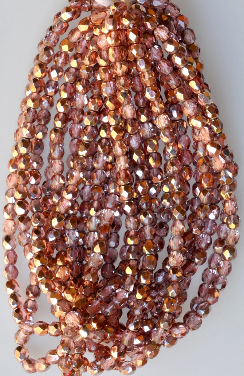 May include: A strand of rose gold glass beads with a faceted finish. The beads are small and have a metallic sheen.