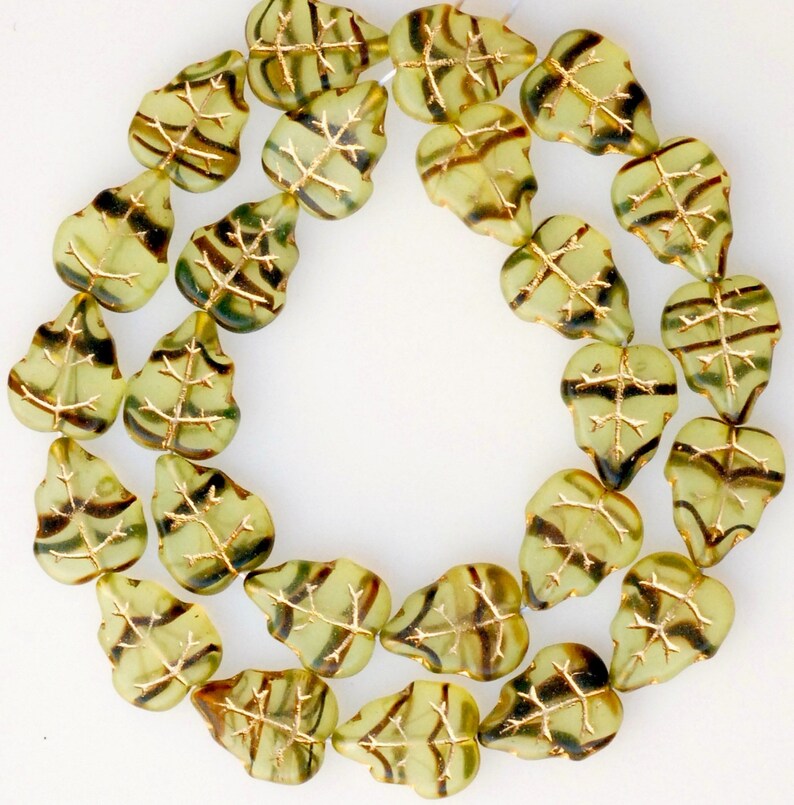 May include: A strand of green glass beads with gold leaf accents. Each bead is shaped like a leaf with a detailed vein pattern.