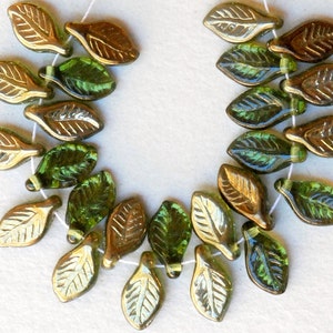 May include: A strand of glass leaf beads in shades of green and gold. The beads are strung on a white thread and have a textured leaf design.