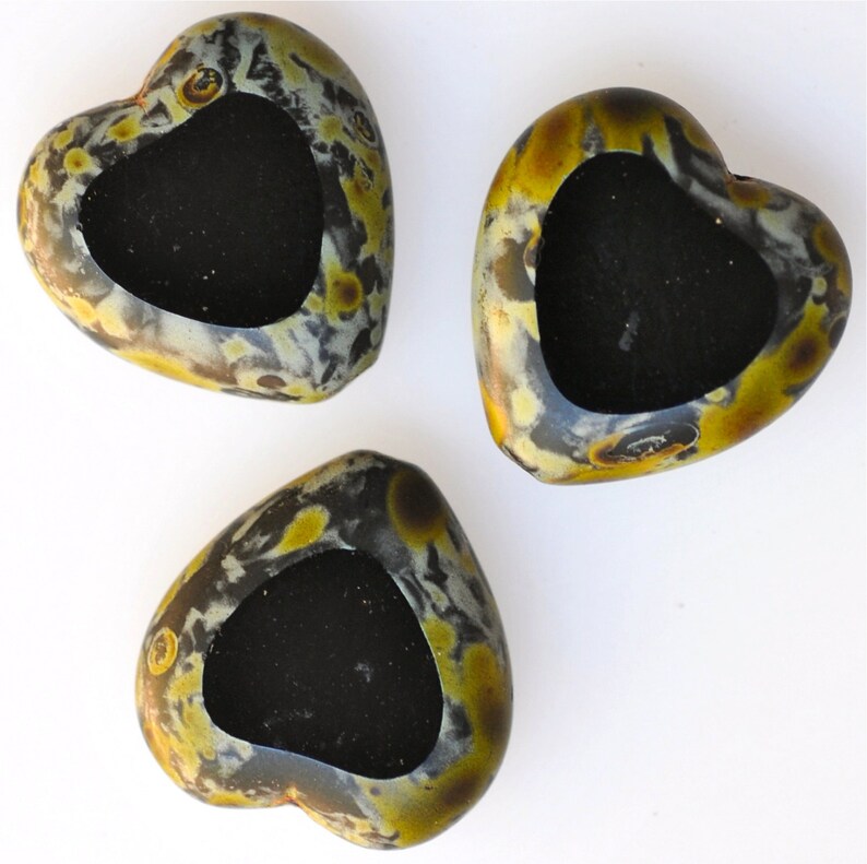 May include: Three heart-shaped candle holders made of black and gold speckled stone. Each holder has a black, heart-shaped cavity in the center.