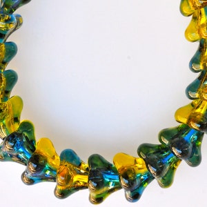 Puede incluir: Un collar hecho de cuentas de vidrio en tonos de amarillo y verde. Las cuentas tienen forma de l&aacute;grima y est&aacute;n enhebradas juntas en un patr&oacute;n repetitivo.