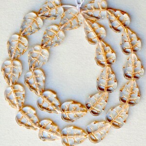 May include: A strand of clear glass beads with gold leaf accents, shaped like leaves. The beads are strung on a white cord.