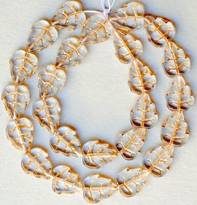 May include: A strand of clear glass beads with gold leaf accents, shaped like leaves. The beads are strung on a white cord.