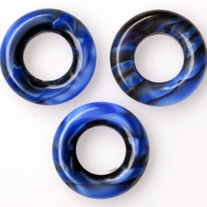 Puede incluir: Tres cuentas de forma de anillo de color azul y negro con un agujero en el centro.