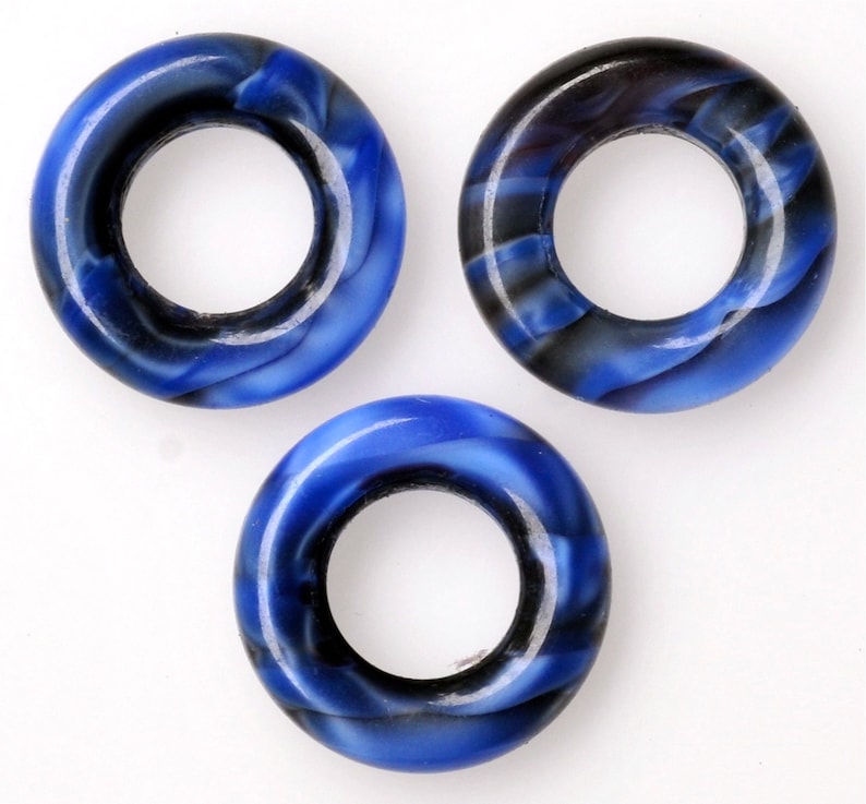 Puede incluir: Tres cuentas de forma de anillo de color azul y negro con un agujero en el centro.