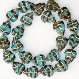 May include: A strand of turquoise and gold leaf glass beads in the shape of leaves. The beads are strung on a clear thread and are arranged in a circle.
