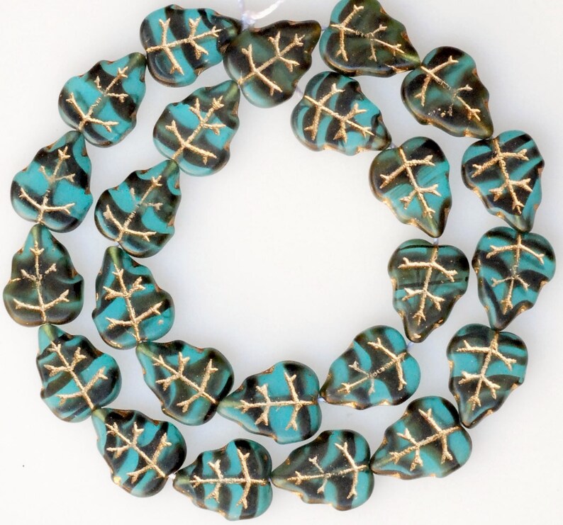 May include: A strand of turquoise and gold leaf glass beads in the shape of leaves. The beads are strung on a clear thread and are arranged in a circle.