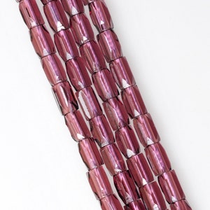 May include: A strand of faceted glass beads in a deep burgundy color. The beads are cylindrical and have a slightly iridescent finish.