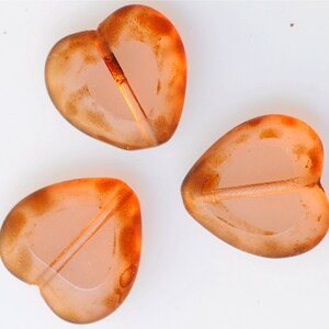 May include: Three heart-shaped glass beads with a translucent orange color and a darker orange rim. The beads have a hole through the center for stringing.