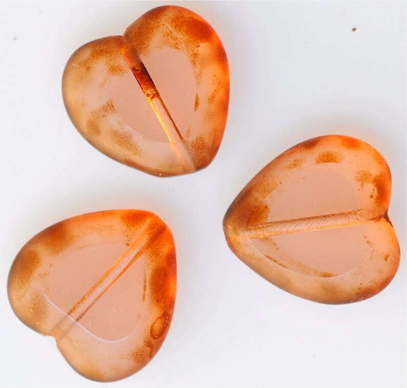 May include: Three heart-shaped glass beads with a translucent orange color and a darker orange rim. The beads have a hole through the center for stringing.