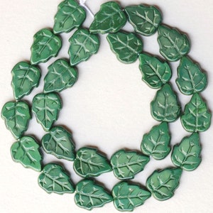 May include: A strand of green glass beads shaped like leaves. The beads are strung together on a white thread.