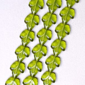 May include: A strand of green glass beads shaped like leaves. The beads are strung on a clear thread and are arranged in a repeating pattern.