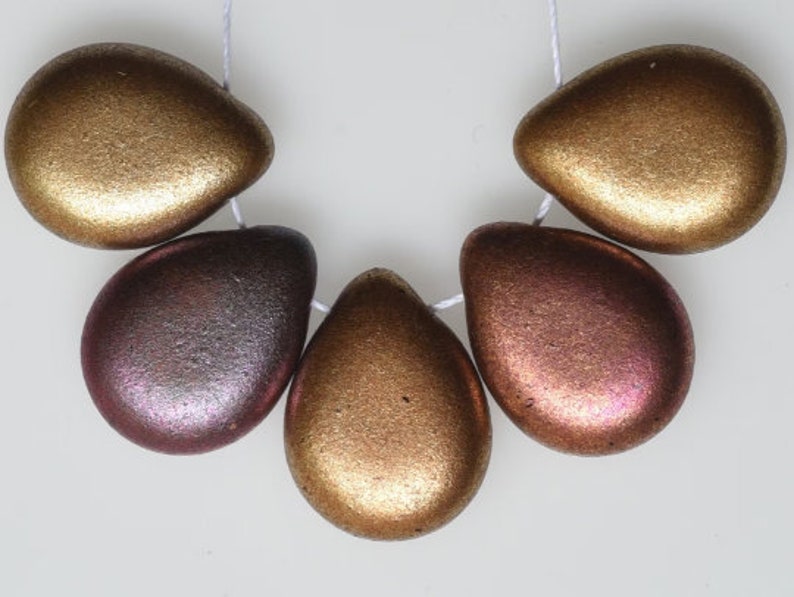 May include: Five metallic teardrop-shaped beads strung on a white cord. The beads have a textured surface and vary in color from gold to bronze and reddish-purple. These beads could be used for jewelry making.