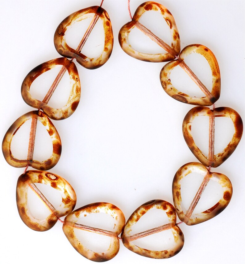 May include: A strand of brown and clear glass heart-shaped beads. The beads have a translucent appearance and are strung together on a thin thread.