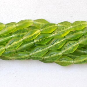 May include: Close-up of strands of translucent, lime green leaf-shaped beads. Each bead has etched leaf vein details. The beads are strung together, creating a textured and organic aesthetic. Ideal for jewelry making.