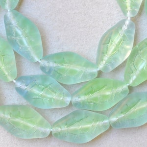 May include: Two strands of translucent leaf-shaped beads in shades of green and blue. The beads are strung on a white cord, and each bead has a detailed leaf vein pattern. The beads are approximately 1 inch long.