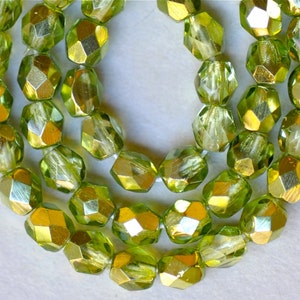 May include: A strand of green glass beads with a metallic gold finish. The beads are faceted and have a slightly irregular shape.