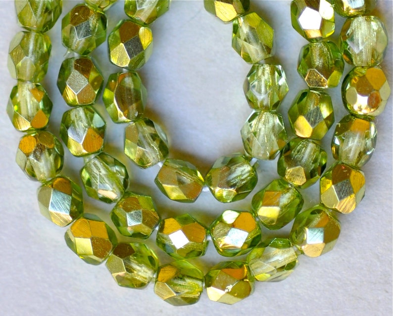 May include: A strand of green glass beads with a metallic gold finish. The beads are faceted and have a slightly irregular shape.
