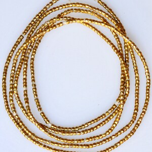 May include: A strand of gold-colored beads, likely made of glass, arranged in a circular pattern. The beads are small and uniform in size, creating a smooth and continuous look.