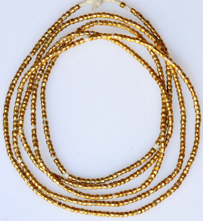 May include: A strand of gold-colored beads, likely made of glass, arranged in a circular pattern. The beads are small and uniform in size, creating a smooth and continuous look.