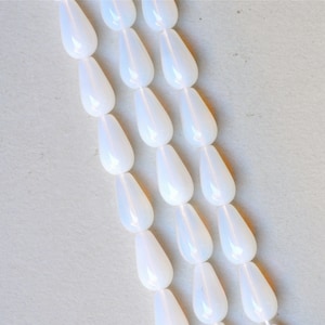 Può includere: Una collana di perle bianche a forma di goccia. Le perle sono infilate su un filo trasparente e sono disposte in file.