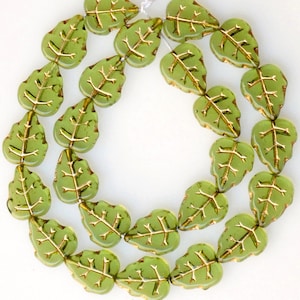 May include: A strand of green glass beads shaped like leaves with gold accents. The beads are strung on a clear thread.