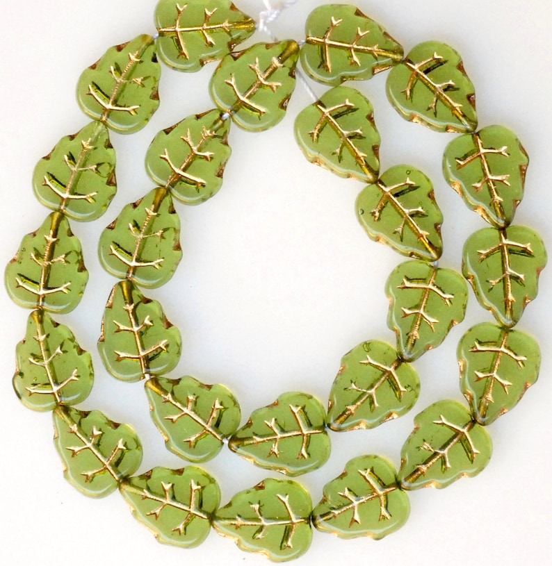 May include: A strand of green glass beads shaped like leaves with gold accents. The beads are strung on a clear thread.