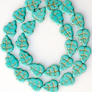 May include: A strand of turquoise blue glass beads in the shape of leaves with gold leaf accents.
