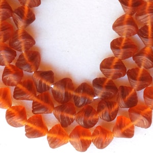 May include: A strand of orange glass beads with a swirl design. The beads are faceted and have a translucent appearance.