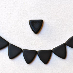 May include: A black necklace made of triangular beads. The necklace is laid out on a white surface.