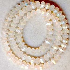 May include: A strand of iridescent white glass beads with a pearlescent finish. The beads are round and have a slightly flattened shape.