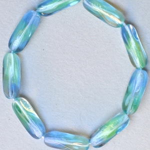 May include: A string of light blue glass beads with iridescent swirls. The beads are oval shaped and have a smooth, polished finish.
