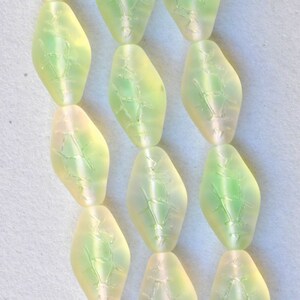 May include: Close-up of several strands of light green, diamond-shaped beads. Each bead has a frosted appearance with a subtle, internal pattern. The beads are strung together, creating a delicate and elegant look.